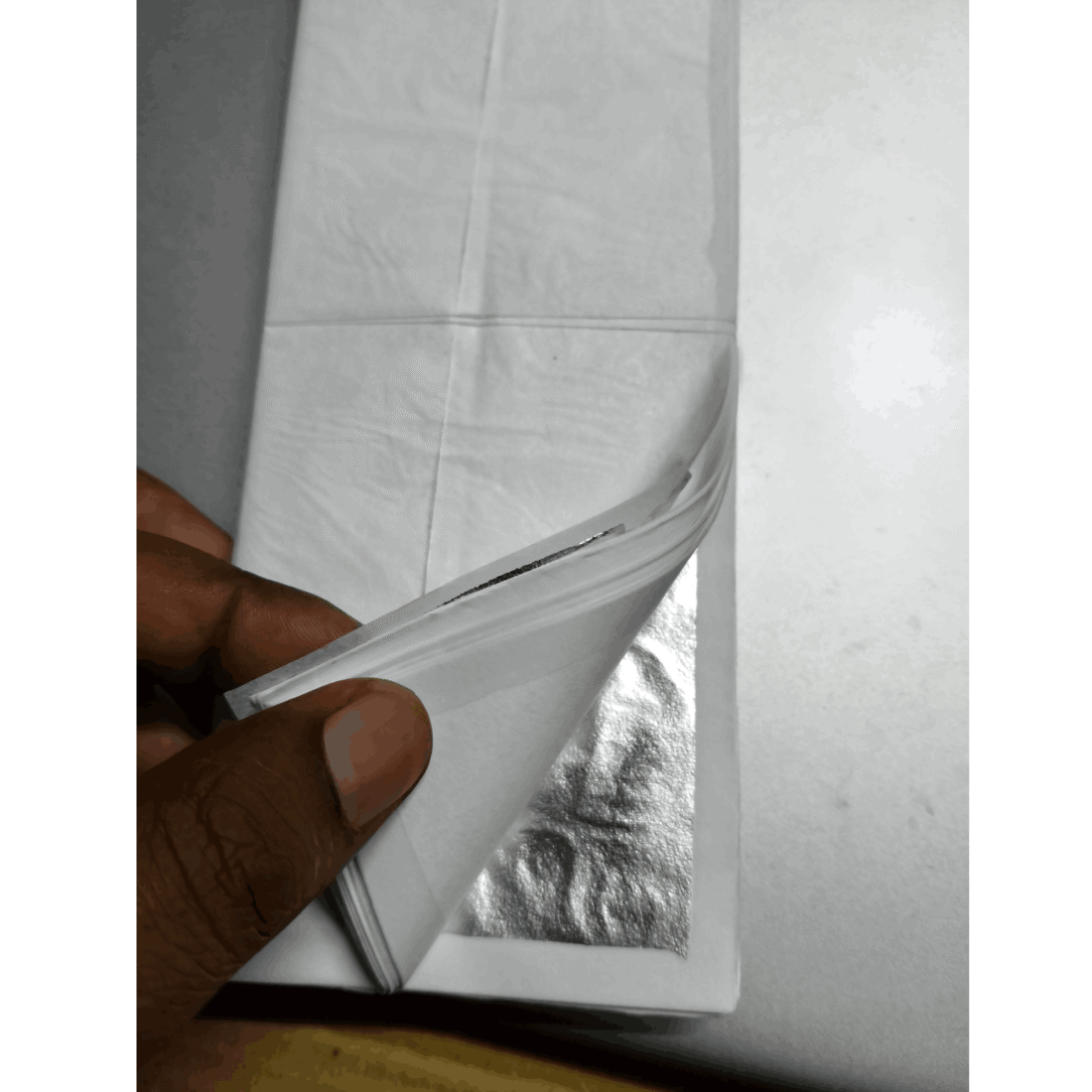 Silver leaf sheet lifted from tissue interleaved booklet by hand