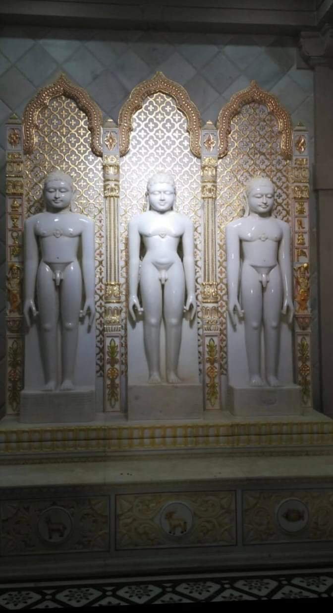 Gold leaf toran arch behind standing Jain murtis