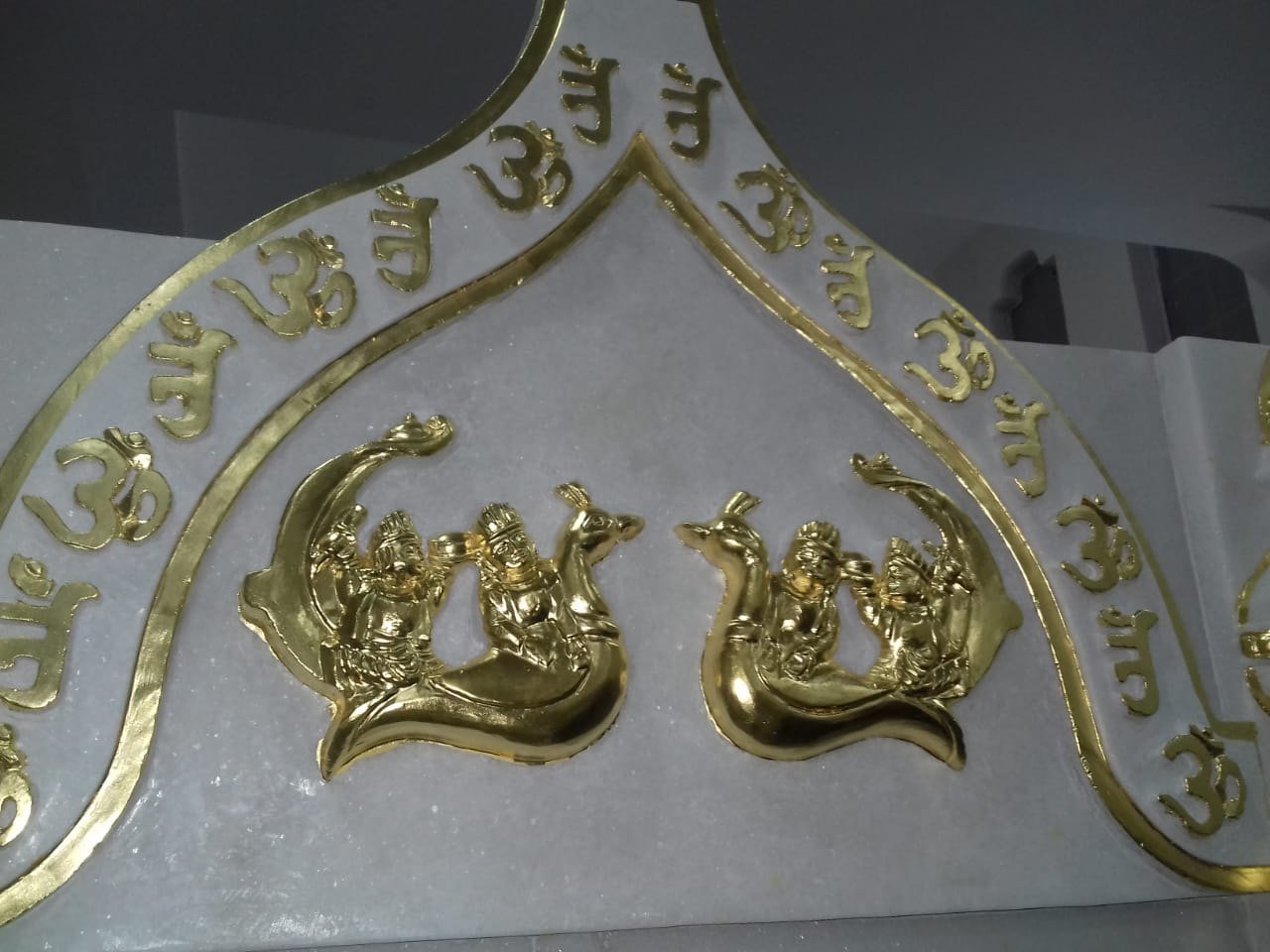 Close-up of gold leaf applied on marble carving with Om lettering and peacock figures