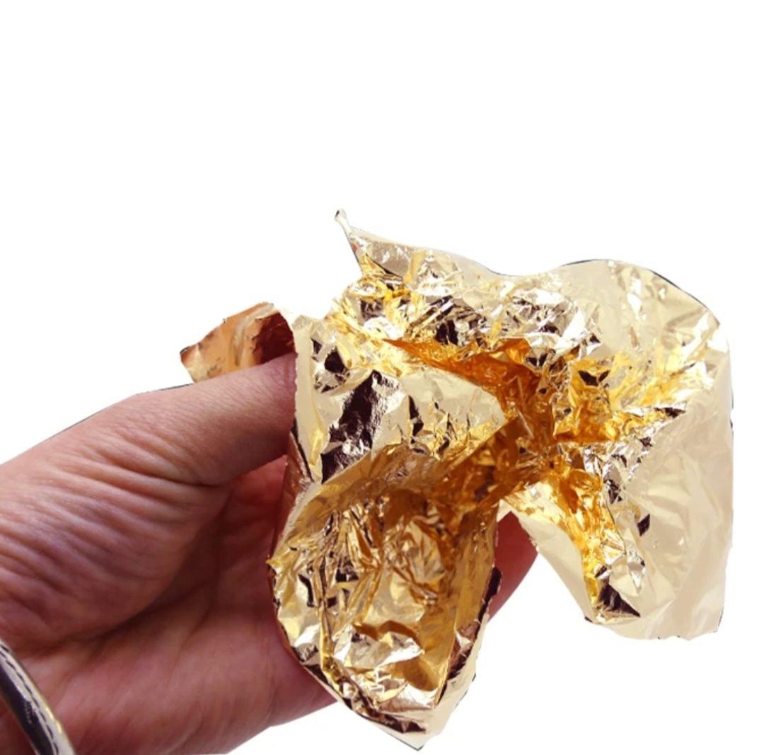 Gold leaf foil sheet held crumpled in hand showing thinness