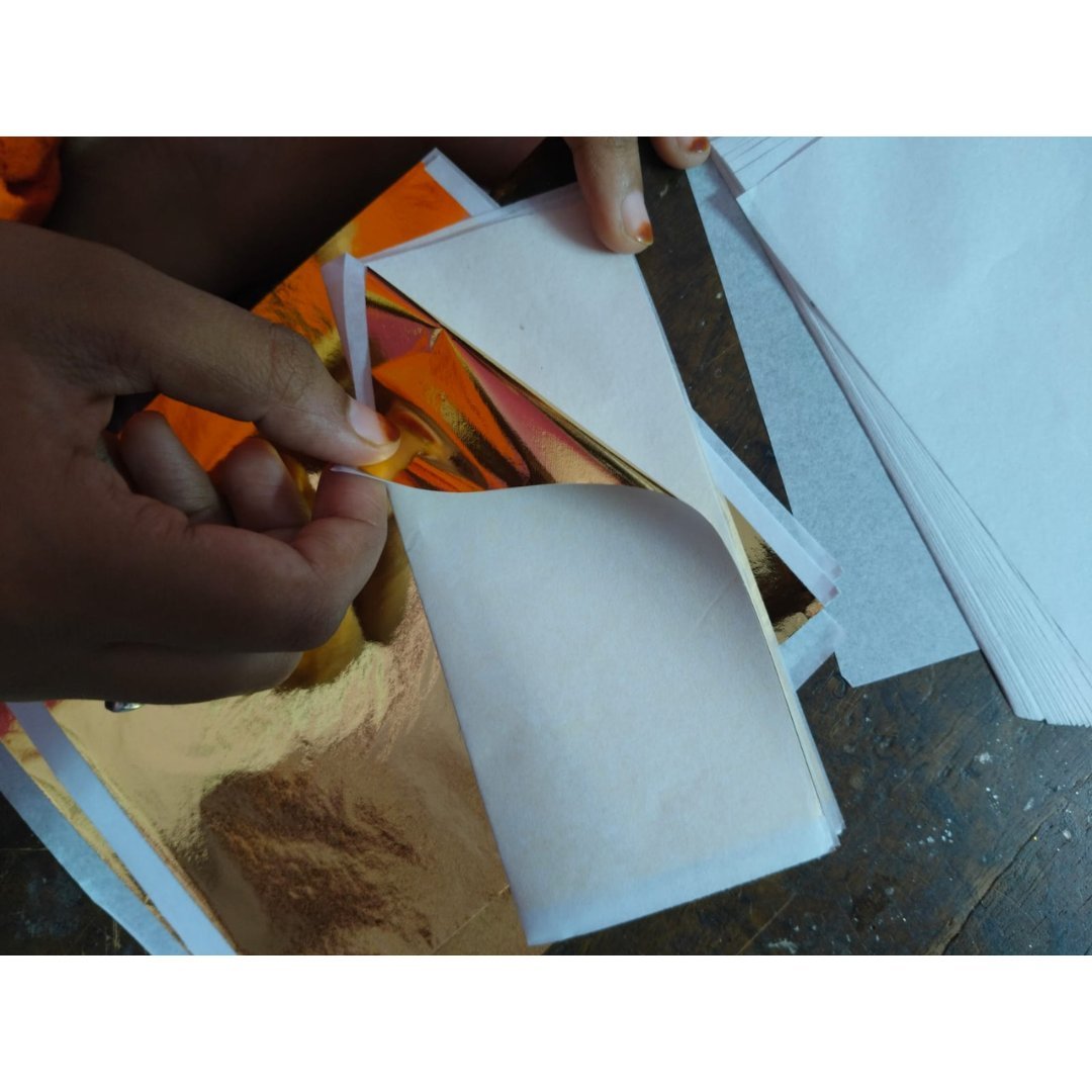Gold leaf foil sheet 14x14 cm being lifted by hand