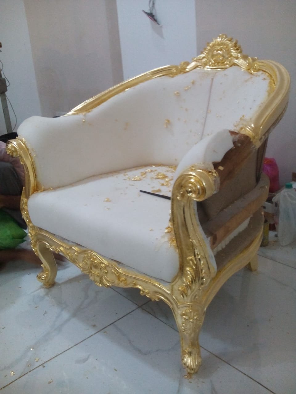 Karigar applying gold leaf by hand on a carved sofa chair frame